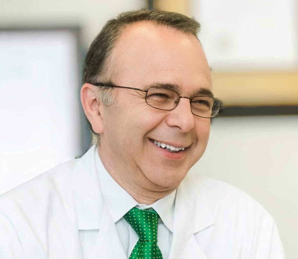A man in glasses and white lab coat smiling.