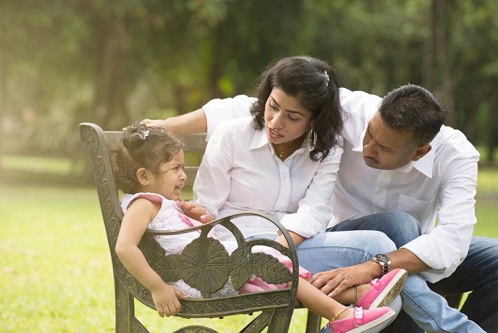 parents comforting crying girl on bench