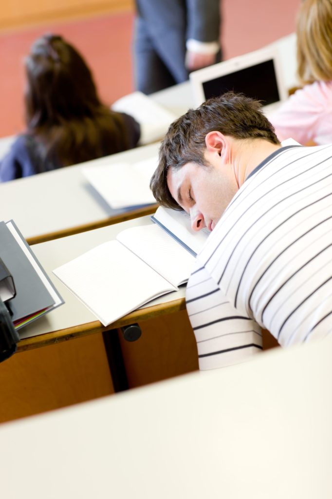 man sleeping on notebook in lecture hall