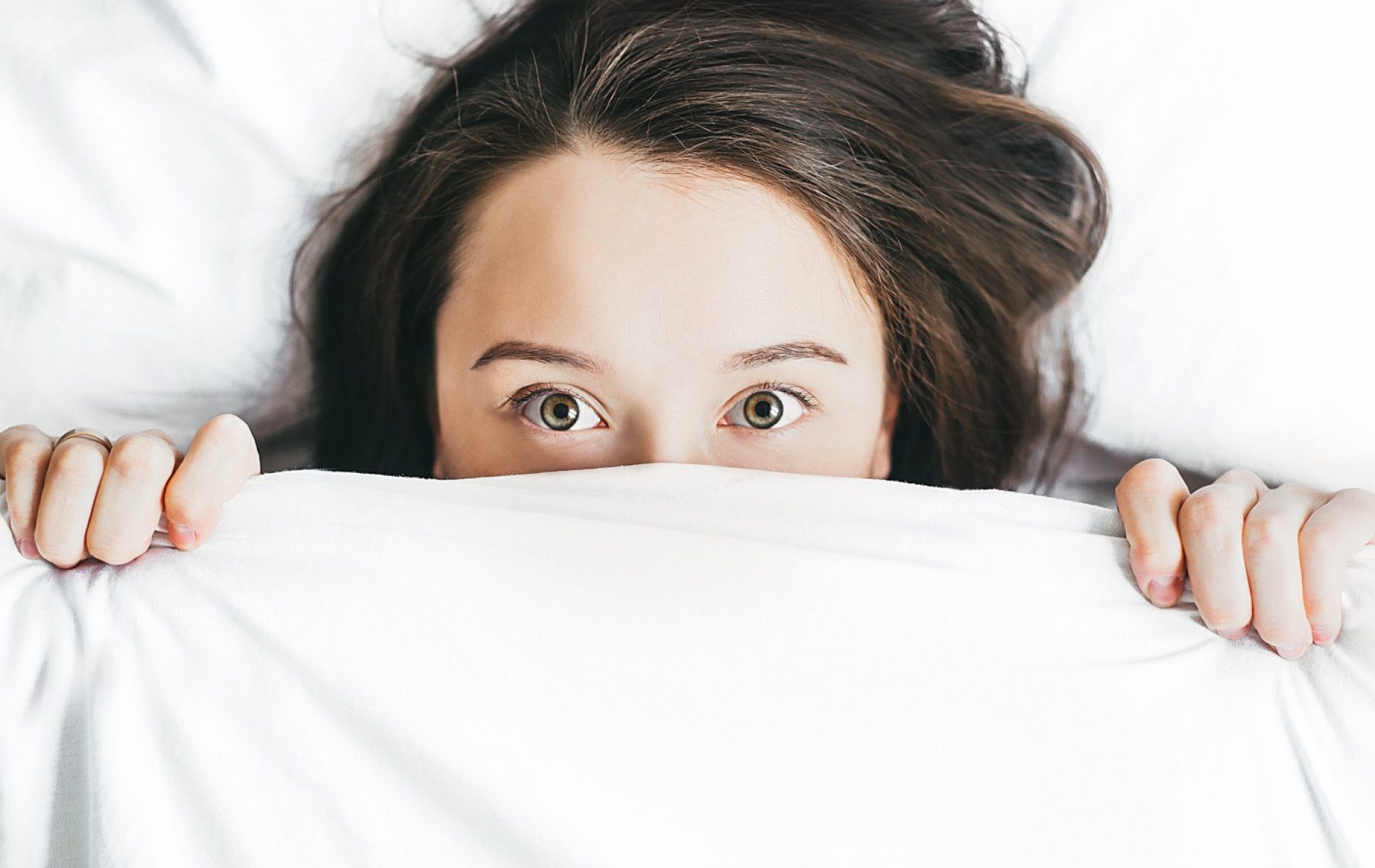 A woman hiding under the covers in bed.